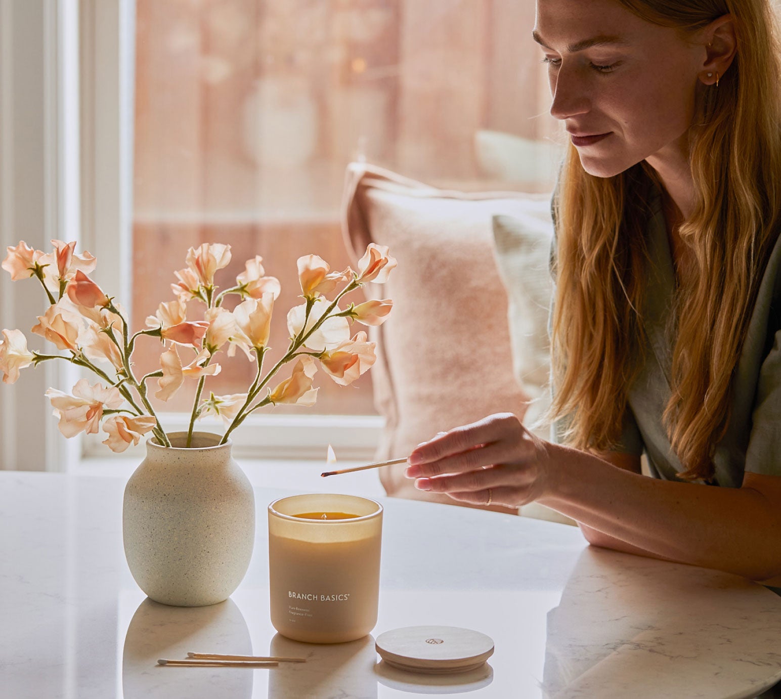 A person uses a lit match to ignite the 100% Beeswax Candle as it sits on a stone tabletop. - View 5
