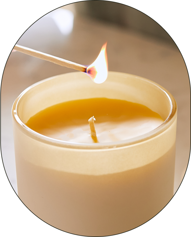 A lit match hovers over the organic cotton wick of a Branch Basics Beeswax Candle.
