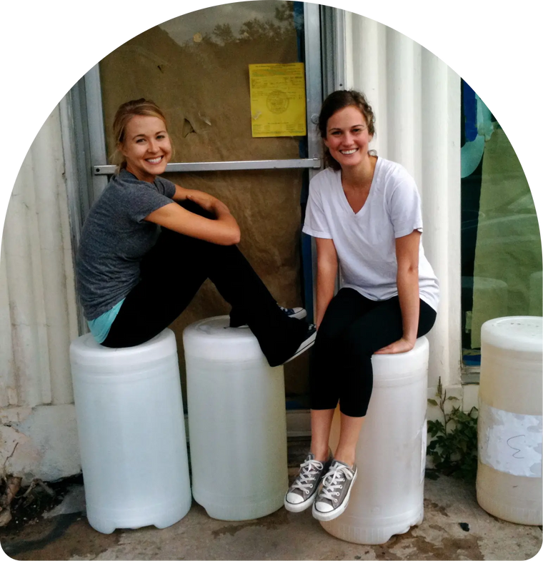 Allison and Kelly sitting on large white cylindrical containers in front of a building entrance.